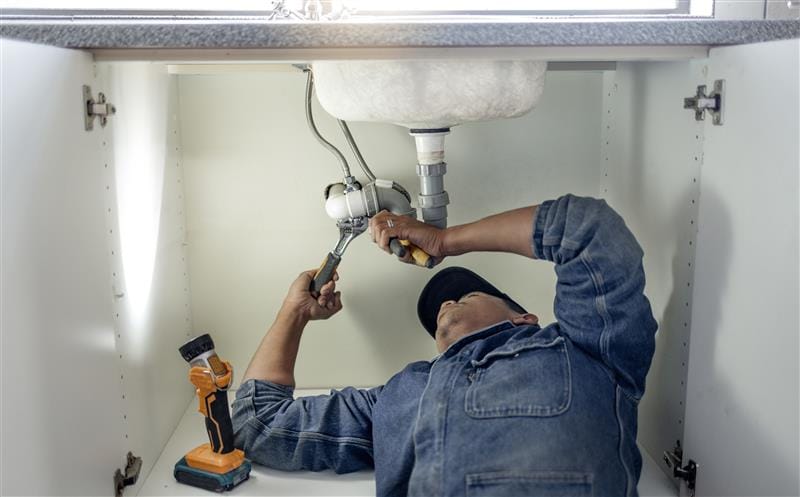 Plumber repairing pipes beneath a bathroom sink in Bethel Park