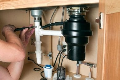 Plumber repairing a garbage disposal beneath a kitchen sink in Bethel Park