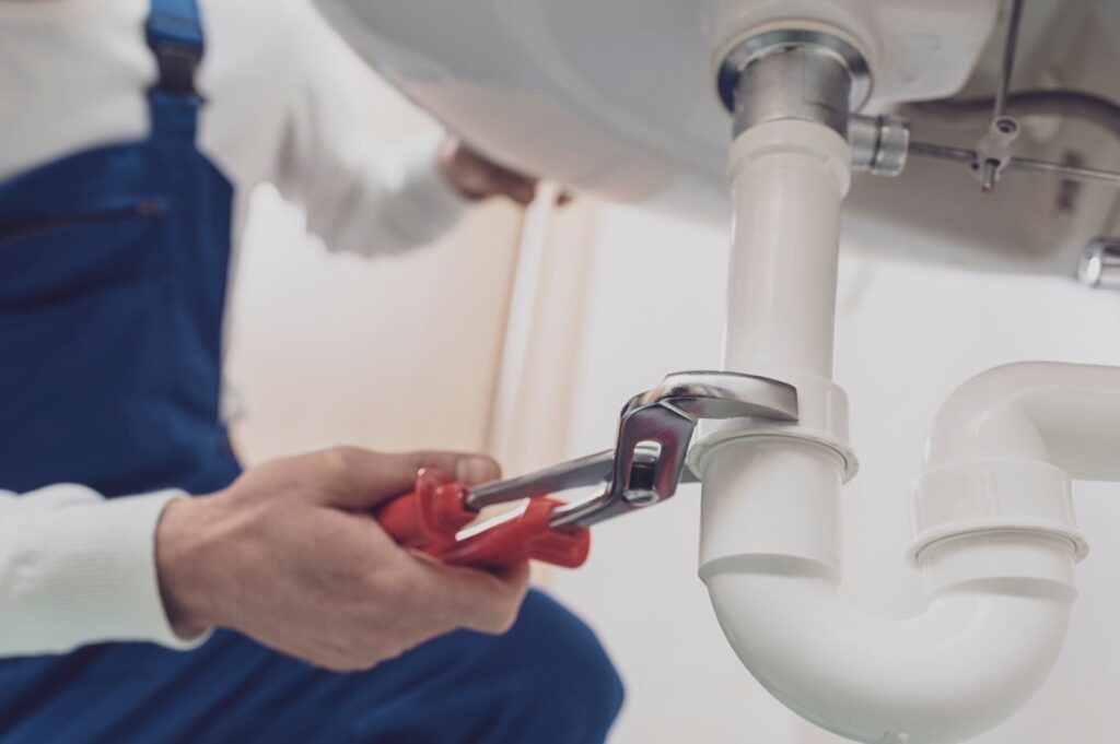 Plumber repairing a white drain pipe beneath a sink in Bethel Park